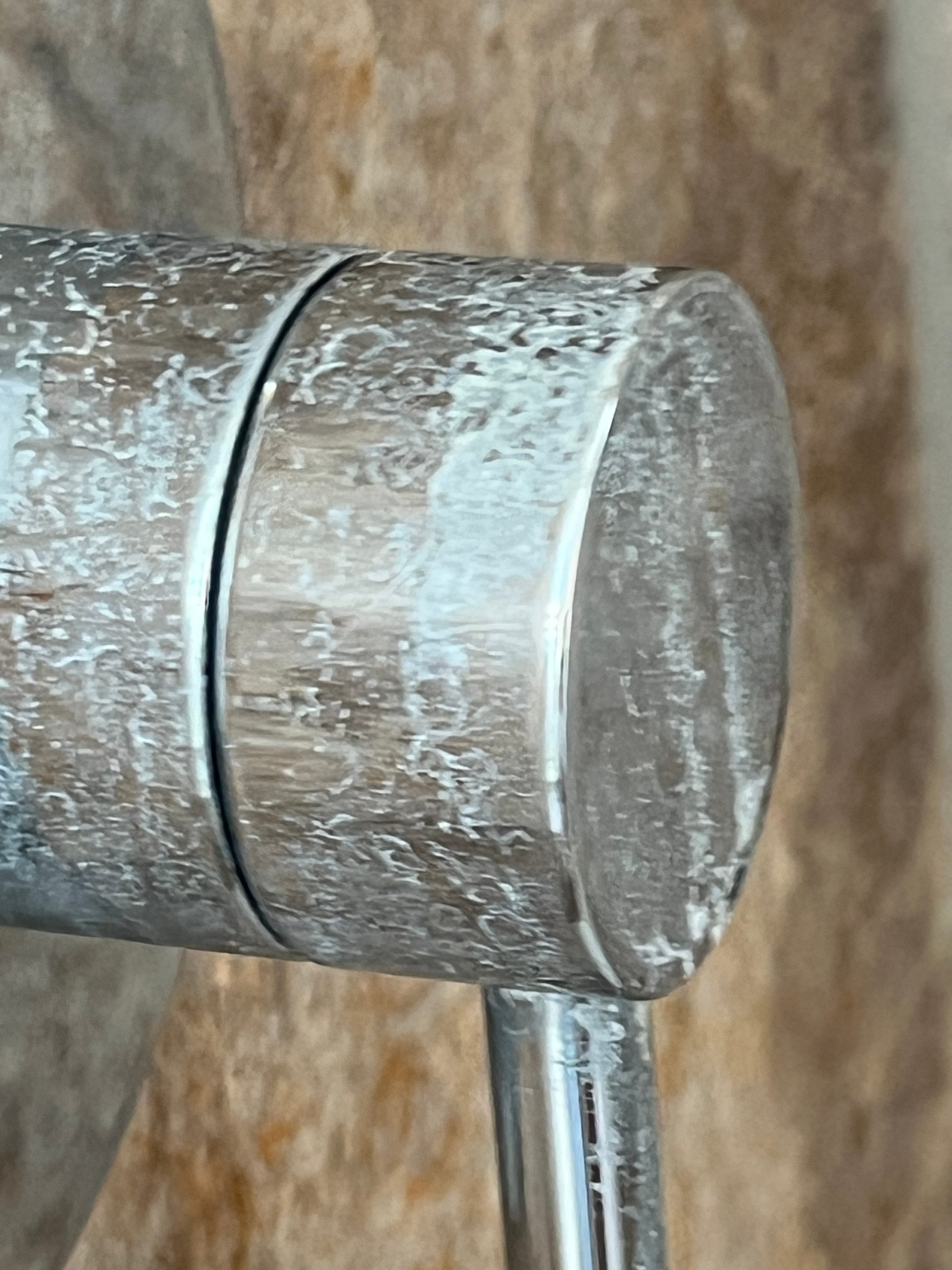 Silver shower handle covered in prominent white hard water stains against a brown tiled wall.