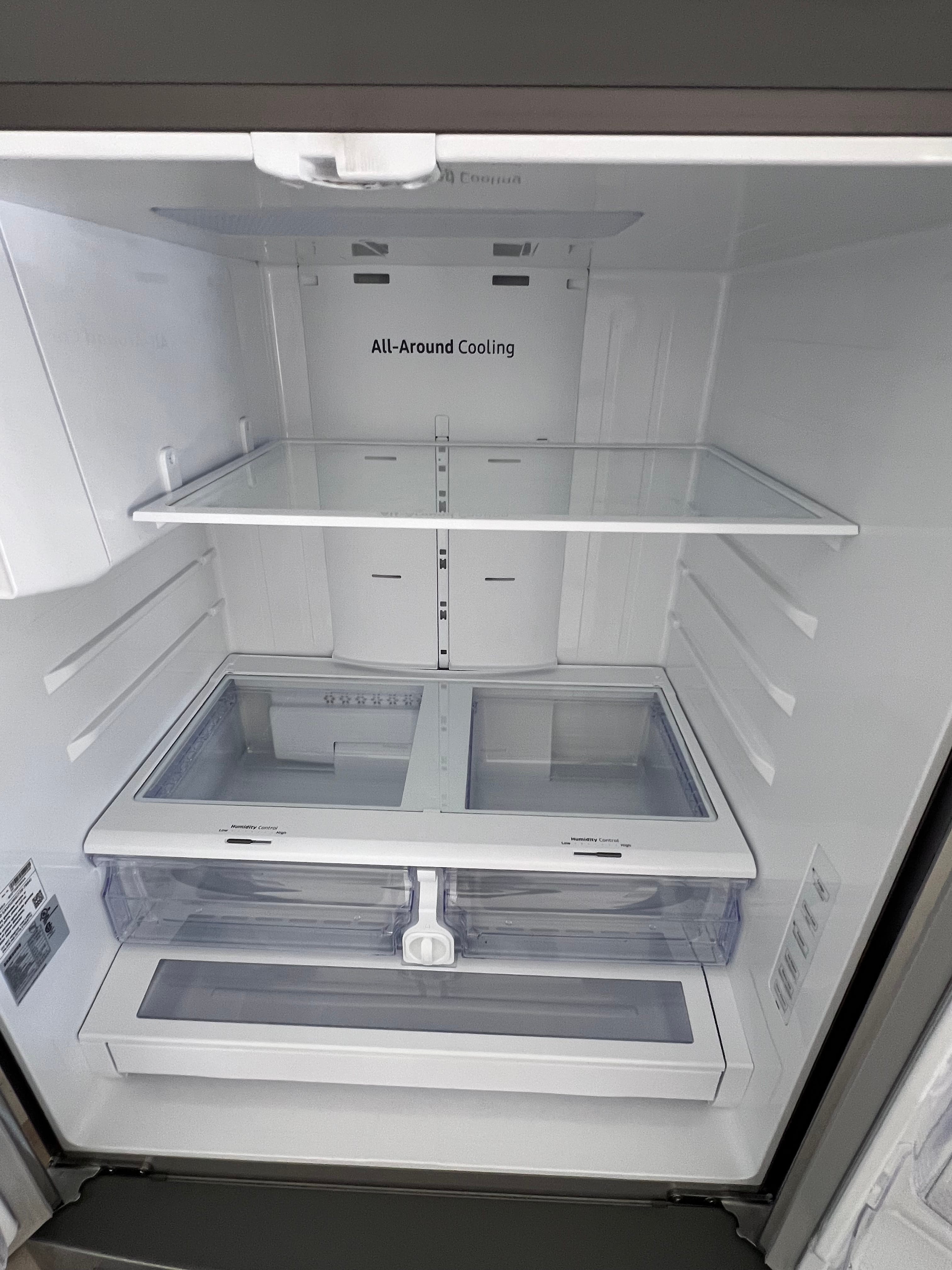Inside a clean, empty refrigerator showing glass shelves, two clear crisper drawers with humidity control, and "All-Around Cooling" text on the back panel.