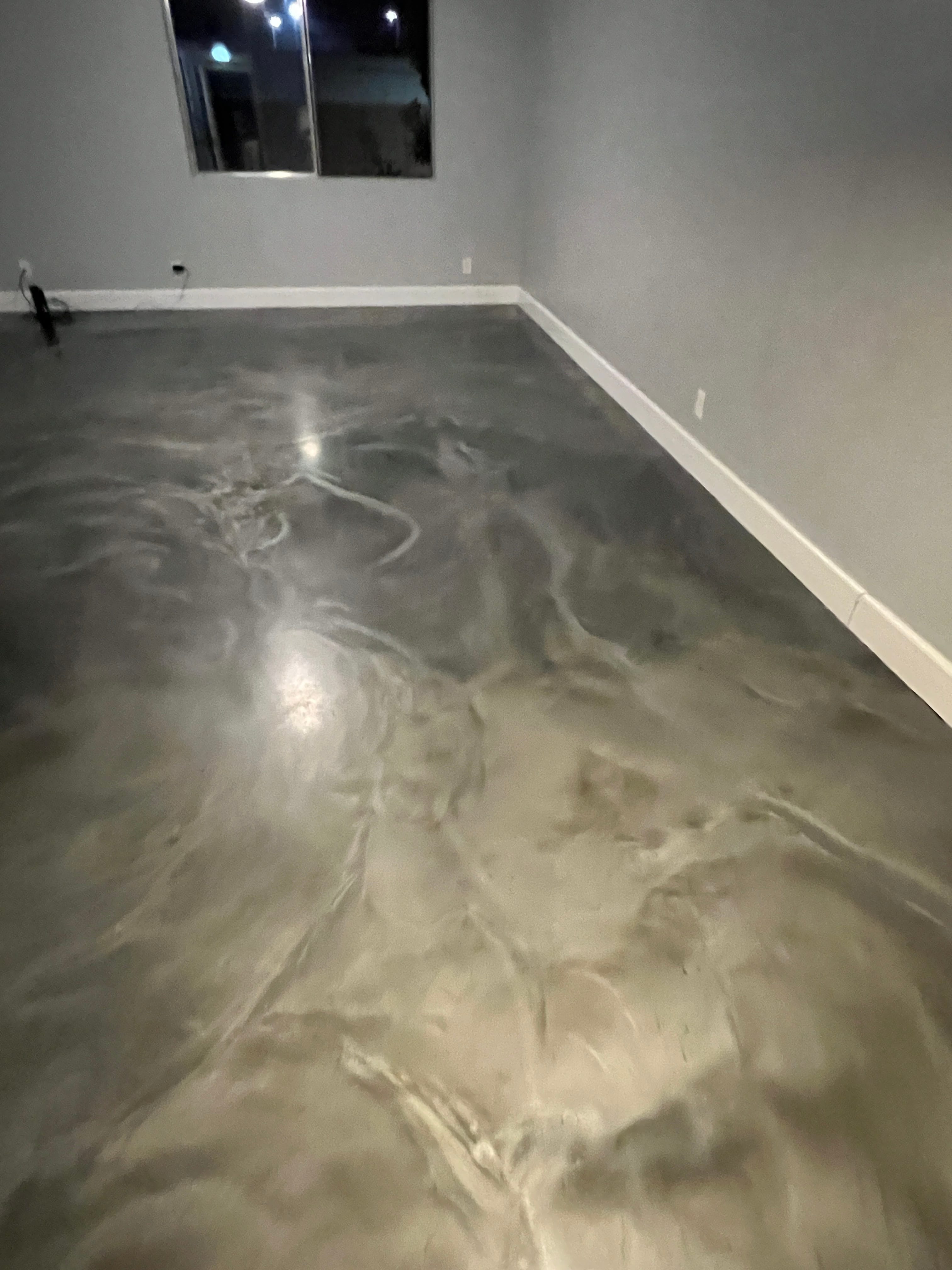 Empty room with a sleek, reflective metallic epoxy floor featuring swirling grey and silver patterns, light grey walls, and white baseboards.