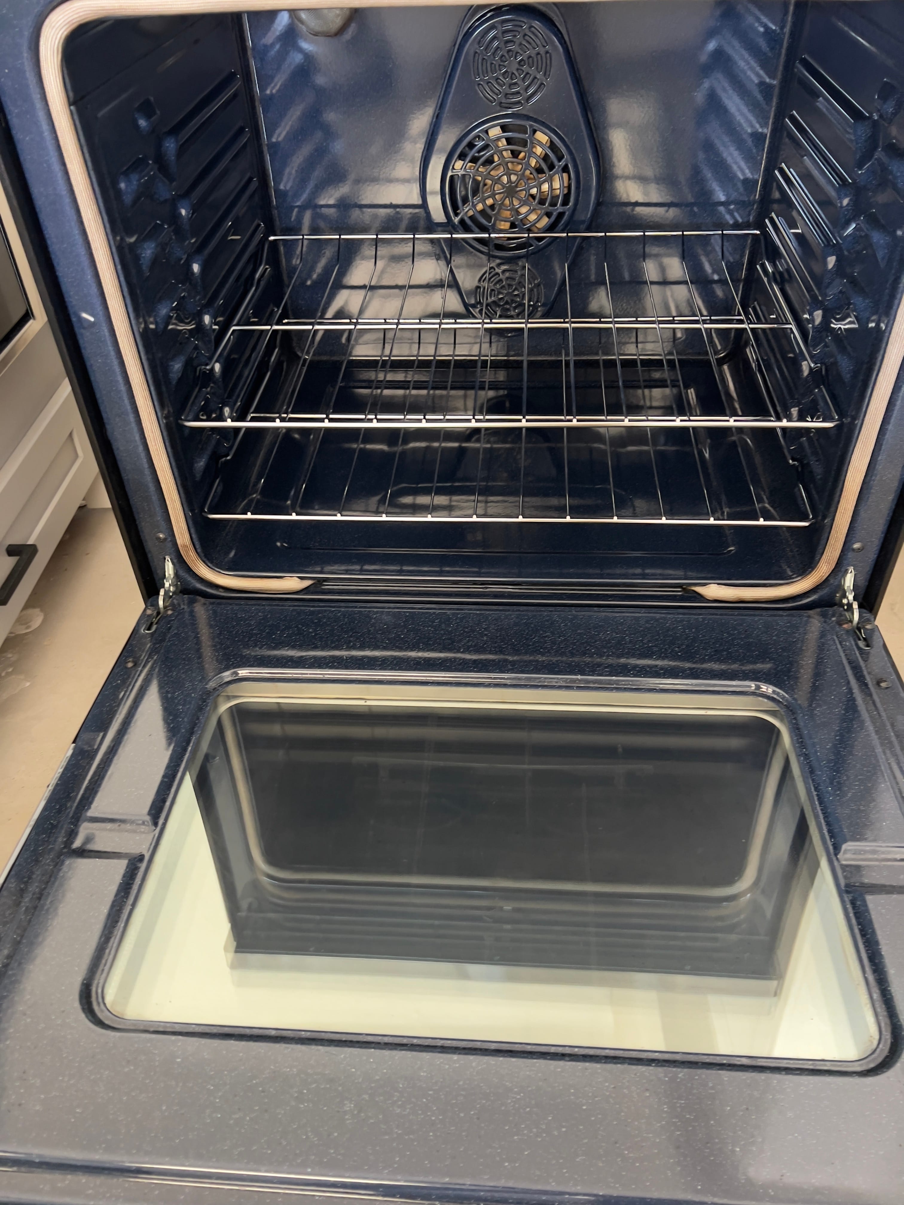 Clean, dark blue oven with the door open, showing two racks and a circular fan with light-colored elements inside at the back.